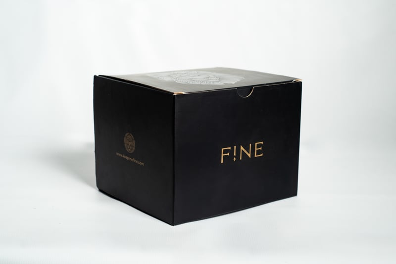 Caja rígida negra premium con branding dorado FINE.