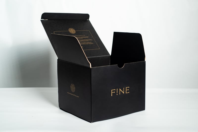 Caja mailer negra abierta de FINE con logo dorado.