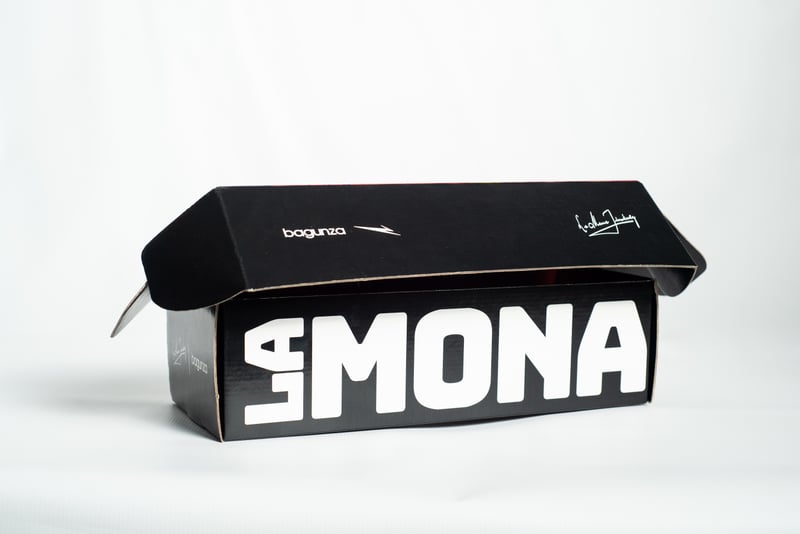 Caja mailer negra cerrada de la colaboración Bagunza × La Mona Jimenez, con texto "LA MONA" en letras blancas grandes.