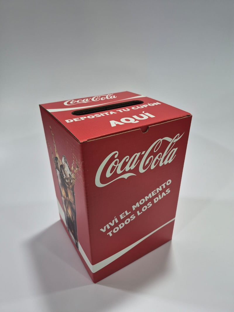 Urna de cartón Coca-Cola para sorteos con ranura superior y leyenda "Deposita tu cupón aquí".