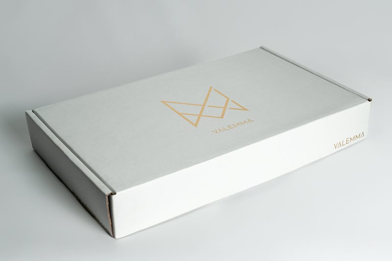 Caja mailer plateada de VALEMMA con logo dorado.