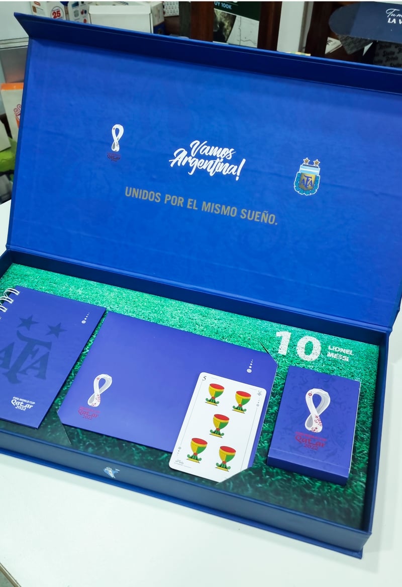 Caja AFA Qatar 2022 abierta con accesorios y fondo césped.